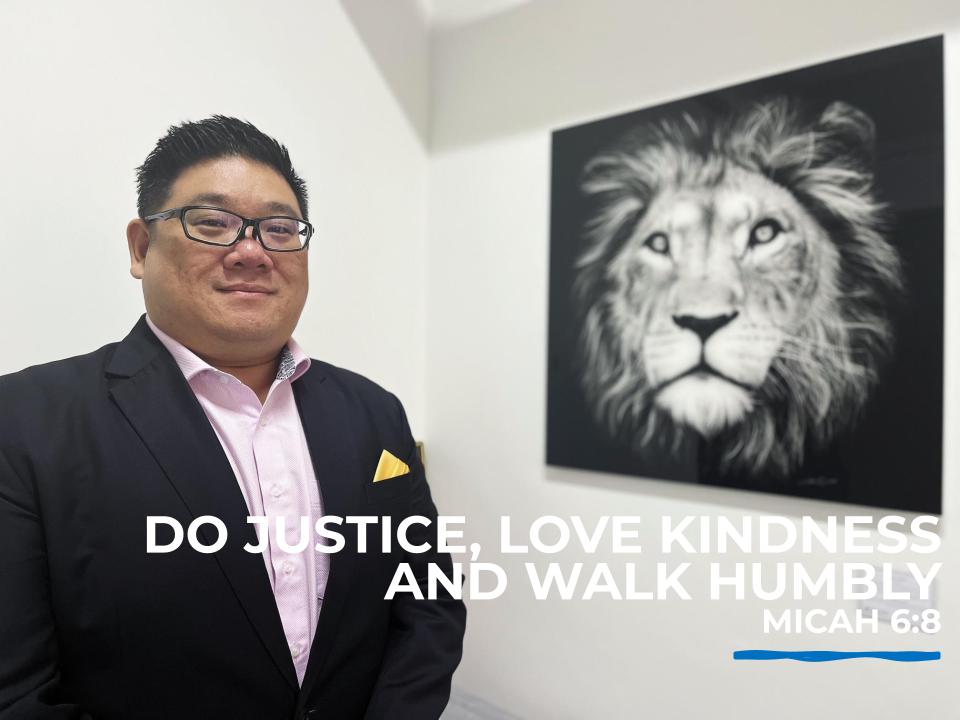 Samuel Yuen, founder and Managing Director of Singapore law firm Yuen Law LLC. Standing in office with an artwork of a lion and the Bible verse "DO JUSTICE, LOVE KINDNESS AND WALK HUMBLY —  MICAH 6:8"